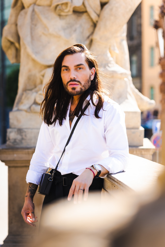Photo by Samuel Galanský: Man in a white shirt and black pants, standing by a stone statue outdoors.